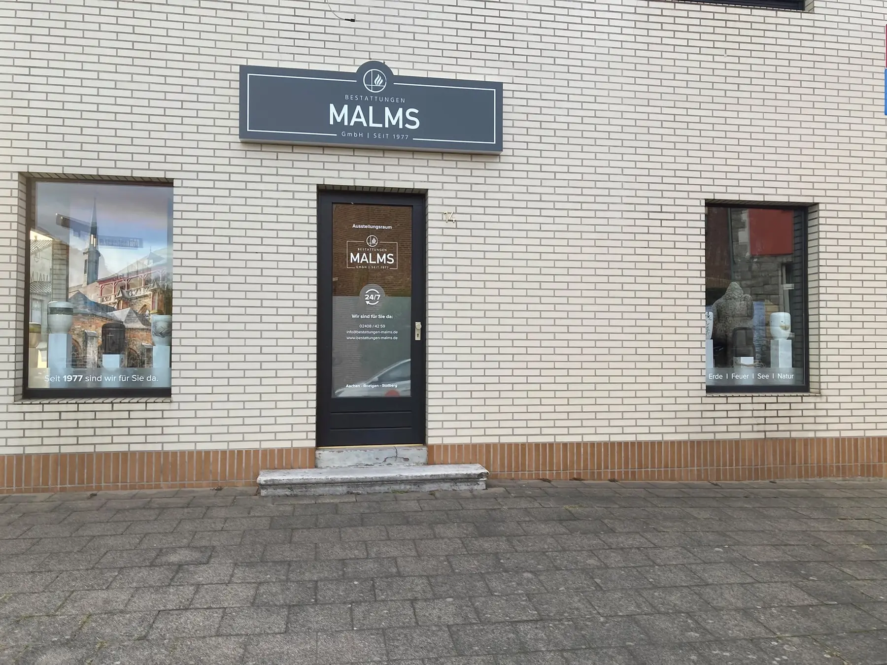 Ladenlokal von Bestattungen Malms mit Schild, Eingangstür zum Ausstellungsraum und zwei Schaufenstern