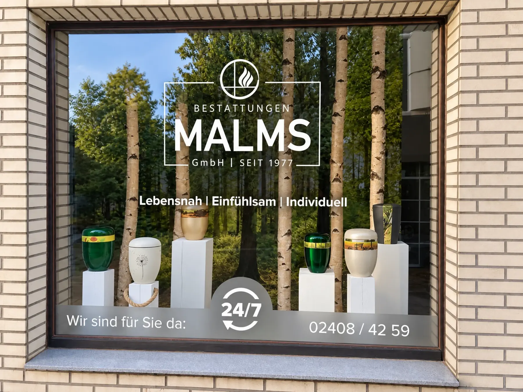 Schaufenster von Bestattungen Malms mit Urnen auf weißen Sockeln vor einem Waldmotiv